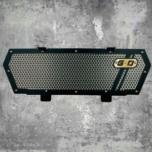 May include: Black metal grille with a honeycomb pattern and a gold G-D logo. The grille is designed to fit over a vehicle's radiator.