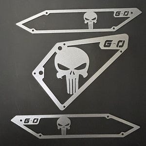 May include: Three metal cutouts of the Punisher skull logo. Each cutout has the text "G-O" in the top right corner. The cutouts are silver in color.