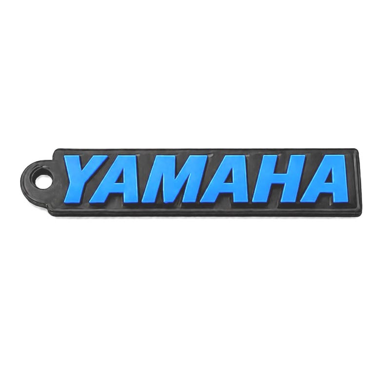 Pu&ograve; includere: Un logo Yamaha nero e blu. La parola "YAMAHA" &egrave; in lettere blu in rilievo su uno sfondo rettangolare nero. Il logo ha un piccolo foro sul lato sinistro.