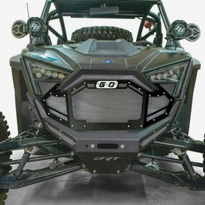 May include: A black off-road vehicle with a custom front grille featuring the text "G-O". The vehicle has LED headlights, a front bumper with the text "DRT", and additional lights mounted on the roll cage.