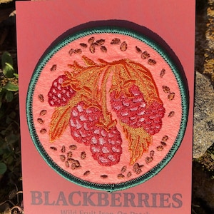 May include: A pink card with a green and brown embroidered patch of blackberries. The text on the card reads "BLACKBERRIES Wild Fruit Iron-On Patch".