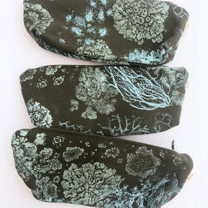 Könnte beinhalten: Drei dunkelgrüne Federmäppchen mit einem hellblauen botanischen Druck. Die Etuis sind rechteckig mit abgerundeten Enden und einem Reißverschluss. Das botanische Design zeigt verschiedene pflanzenartige Formen.