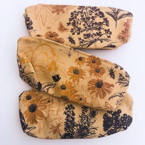 Könnte beinhalten: Drei beige Federmäppchen mit floralen und Insektenmustern in Braun und Schwarz. Die Designs umfassen Blumen, Blätter und Schmetterlinge. Jedes Etui hat einen Reißverschluss.