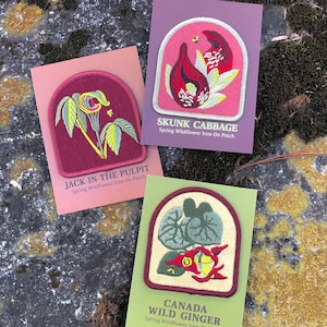 May include: Three iron-on patches featuring illustrations of spring wildflowers. The patches are on cards with the names "Jack-in-the-Pulpit", "Skunk Cabbage", and "Canada Wild Ginger".