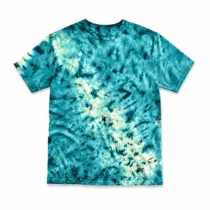 May include: A short-sleeve crew neck t-shirt featuring a tie-dye pattern in shades of teal, dark blue, and white. The design displays a diagonal band of lighter, cream-colored tones running from the upper left shoulder toward the lower right hem.