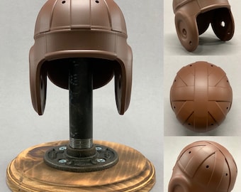 Op de afbeelding: Een bruine voetbalhelm met een vintage ontwerp. De helm staat op een houten standaard met een metalen pijp.
