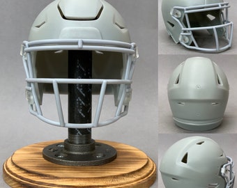 Op de afbeelding: Een grijze voetbalhelm met een gezichtsmasker wordt getoond op een houten standaard met een zwarte metalen pijpbasis.
