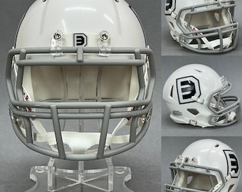 May include: White football helmet with a gray face mask and a black letter "E" on the side. The helmet is on a clear acrylic display stand.