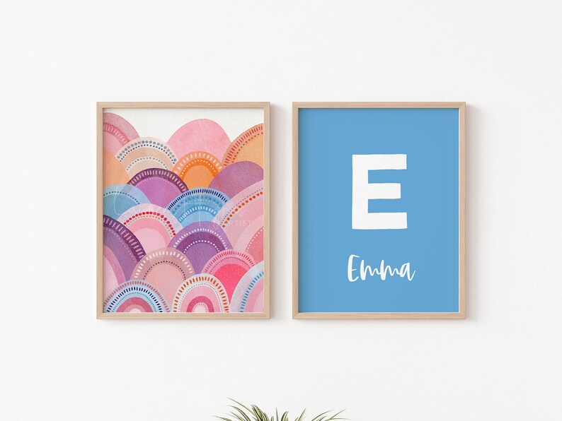 May include: Two framed art prints. One features a watercolour design of layered, semi-circular shapes in shades of pink, orange, purple, and blue. The other has a light blue background with a white letter "E" and the name "Emma" in script.