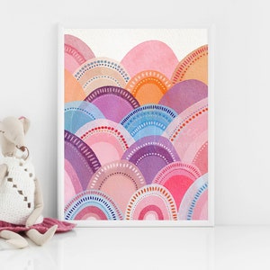 May include: A framed watercolour print depicting an abstract landscape. The artwork features layered, semi-circular shapes in pink, purple, orange, and blue hues. The print is displayed in a white frame and set against a white background.