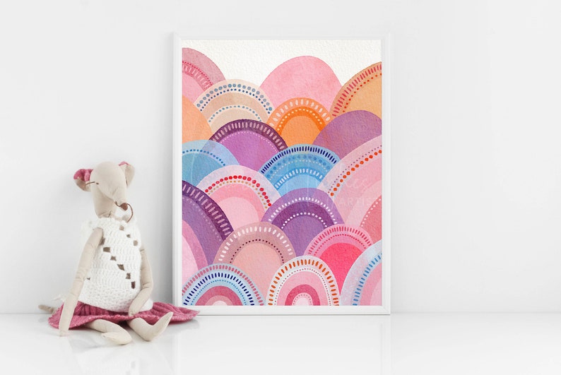 May include: A framed watercolour print depicting an abstract landscape. The artwork features layered, semi-circular shapes in pink, purple, orange, and blue hues. The print is displayed in a white frame and set against a white background.