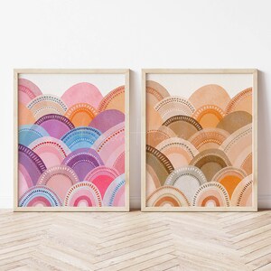 May include: Two framed watercolour prints. One shows a colourful array of pink, purple, blue, and orange semi-circles with dotted details. The other displays a similar design in warm earth tones of brown, tan, and orange. Both are in light wood frames.