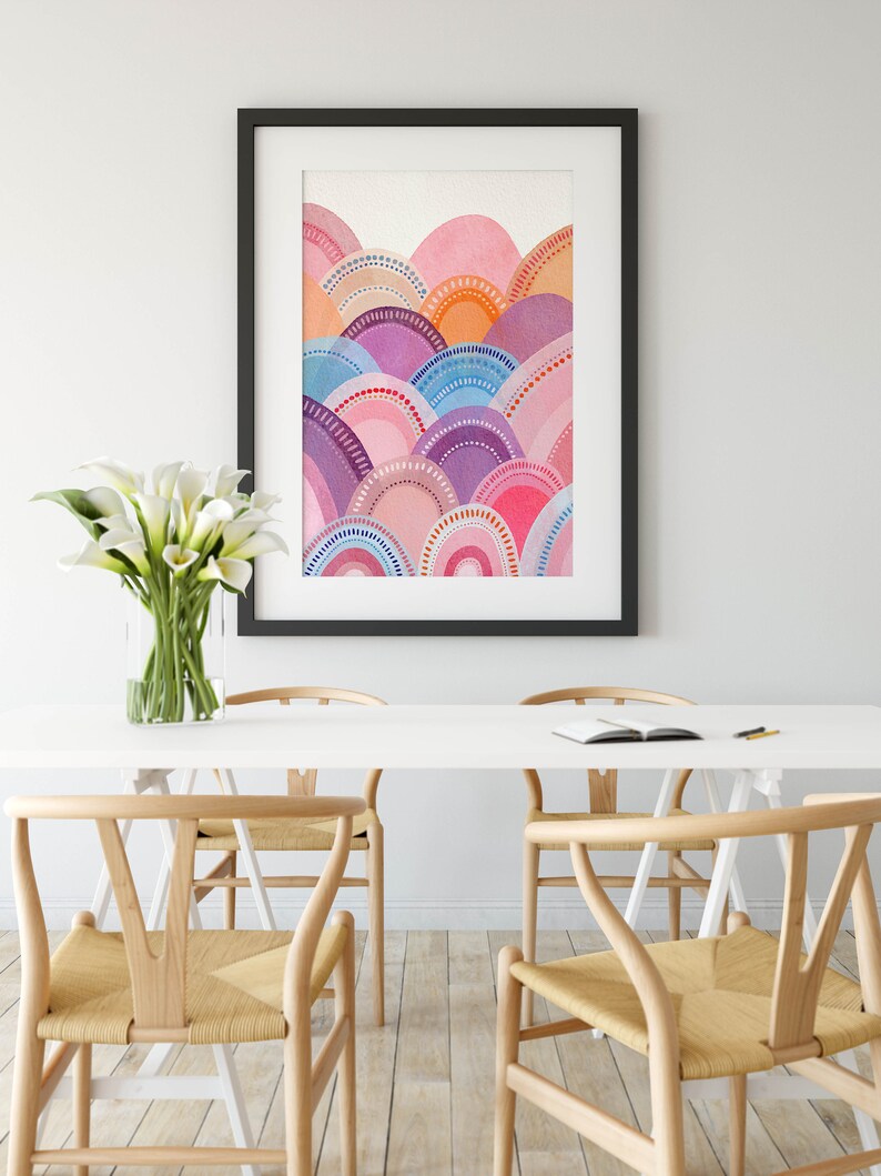 May include: A framed watercolour print with an abstract design of layered, semi-circular shapes in pink, purple, blue, and orange. The artwork is in a black frame, adding a modern touch. The room also features a white table and wooden chairs. The table is 150 cm long.