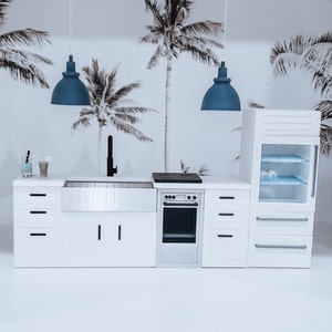 May include: A white kitchen with a stainless steel sink, a white oven, and a white refrigerator. The kitchen has a black faucet and a black stovetop. There are two blue pendant lights hanging above the sink.