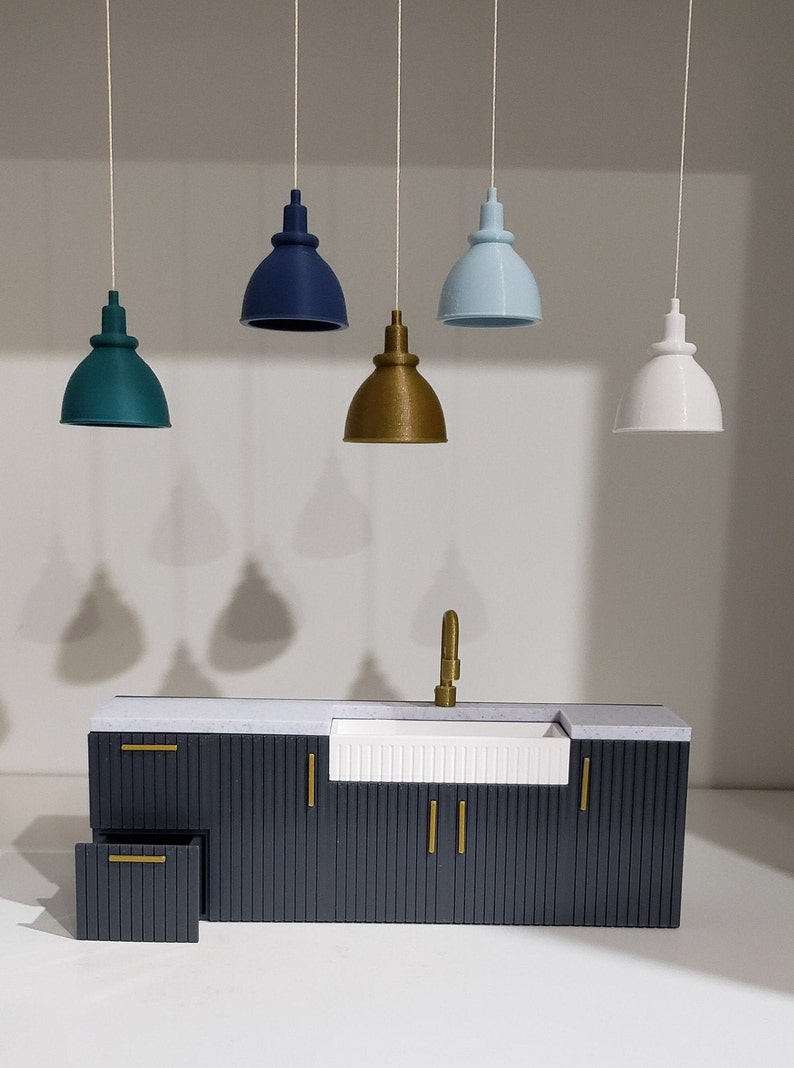 May include: A dark gray kitchen cabinet with a white farmhouse sink and gold hardware. Five pendant lights hang above the cabinet, including teal, blue, gold, and white.
