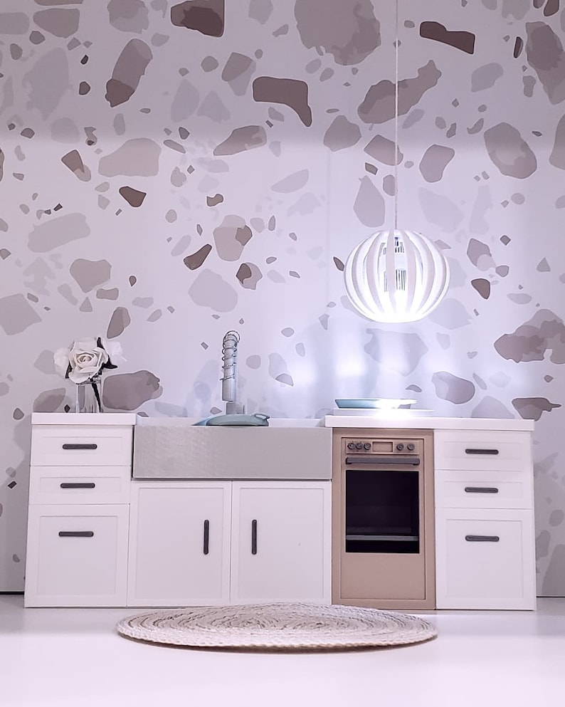 May include: White kitchen cabinets with a farmhouse sink, a brown oven, and a white round pendant light hanging above. The cabinets have black handles and the backsplash is a white and brown terrazzo pattern.