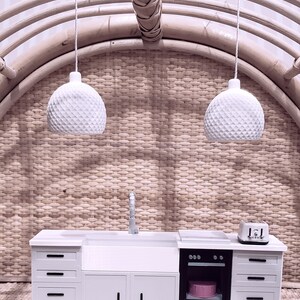 May include: A miniature white kitchen set with a sink, oven, and cabinets. The set is made of wood and has a white finish. The kitchen is set against a woven background.
