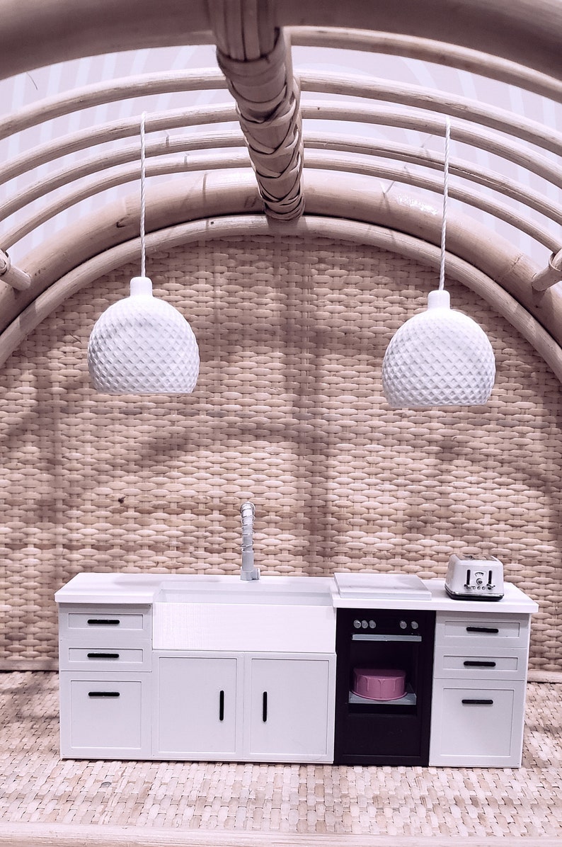 May include: A miniature white kitchen set with a sink, oven, and cabinets. The set is made of wood and has a white finish. The kitchen is set against a woven background.