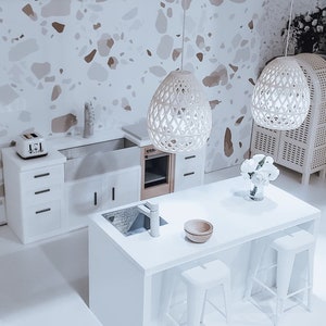 May include: A white kitchen island with a white countertop, a sink, and a faucet. Two white metal bar stools are positioned on either side of the island. The island is in front of a white kitchen with white cabinets and a white tiled backsplash. Two white pendant lights hang above the island.