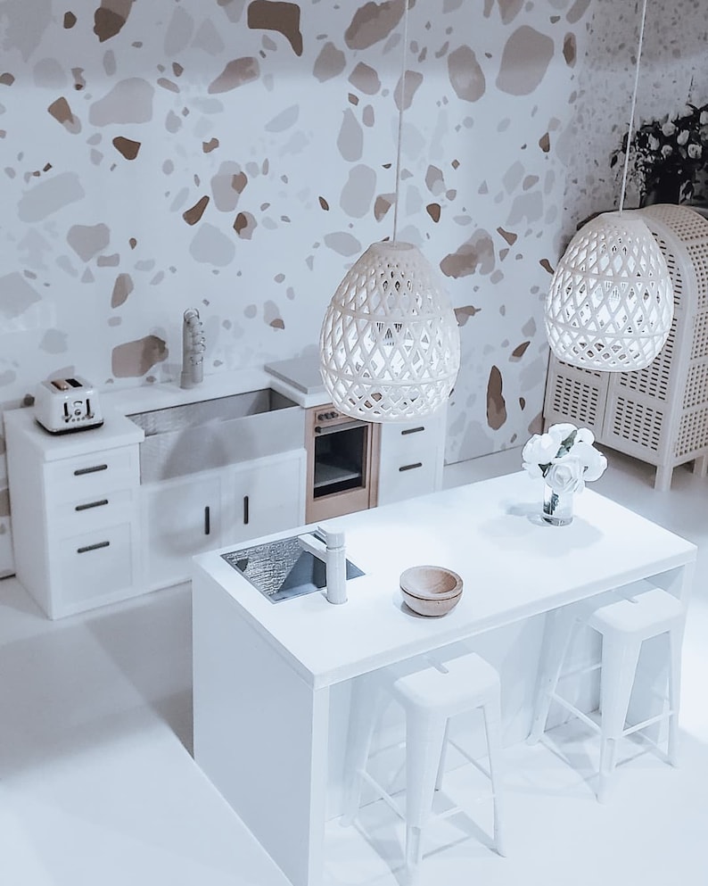 May include: A white kitchen island with a white countertop, a sink, and a faucet. Two white metal bar stools are positioned on either side of the island. The island is in front of a white kitchen with white cabinets and a white tiled backsplash. Two white pendant lights hang above the island.