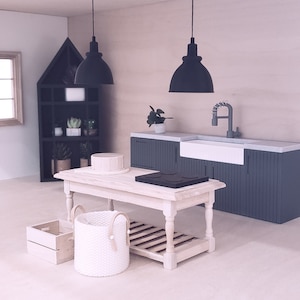 May include: A miniature kitchen set featuring a white farmhouse style table, a white wicker basket, a wooden crate, a black stovetop, and a grey kitchen sink with a black tap.