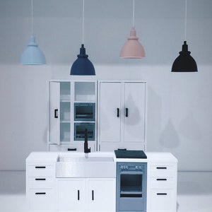 May include: A white miniature kitchen set with a sink, stove, oven, and cabinets. The set includes three hanging light fixtures, one blue, one pink, and one black.