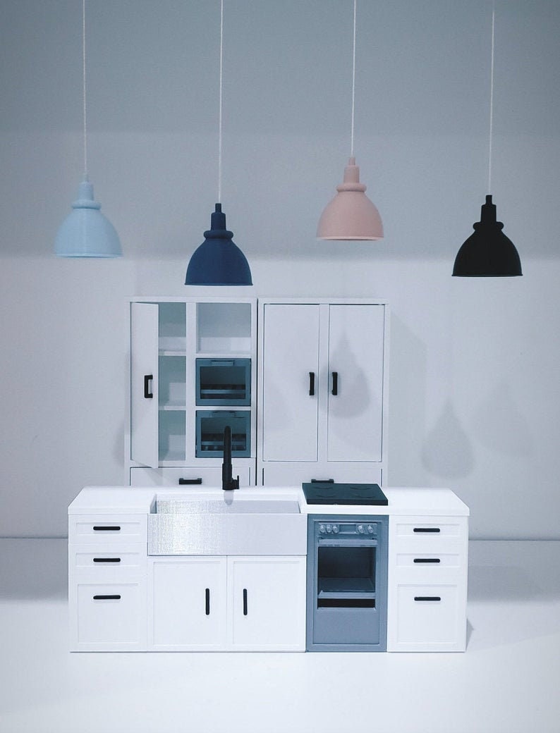 May include: A white miniature kitchen set with a sink, stove, oven, and cabinets. The set includes three hanging light fixtures, one blue, one pink, and one black.