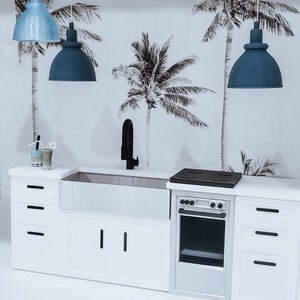 May include: A white kitchen with a farmhouse sink, a black faucet, a white oven with a black stovetop, and three blue pendant lights hanging from the ceiling. The wall behind the kitchen is decorated with a tropical palm tree wallpaper.