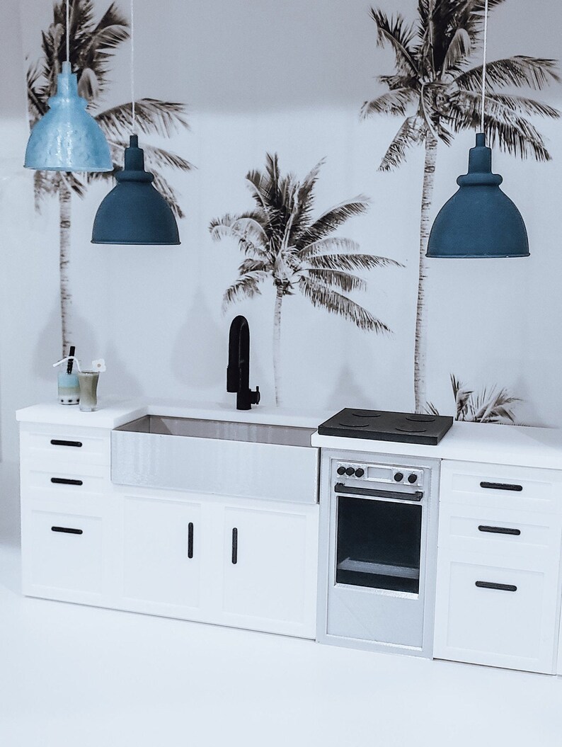 May include: A white kitchen with a farmhouse sink, a black faucet, a white oven with a black stovetop, and three blue pendant lights hanging from the ceiling. The wall behind the kitchen is decorated with a tropical palm tree wallpaper.