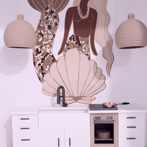 May include: A white kitchen playset with a brown oven, a sink, and three drawers. The backsplash features a mermaid illustration with a seashell and two light fixtures.