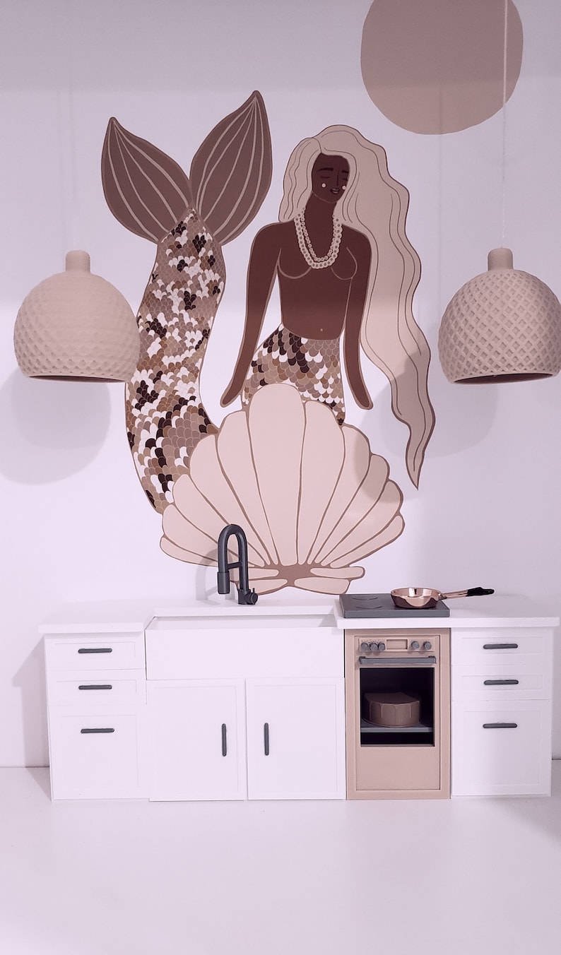 May include: A white kitchen playset with a brown oven, a sink, and three drawers. The backsplash features a mermaid illustration with a seashell and two light fixtures.