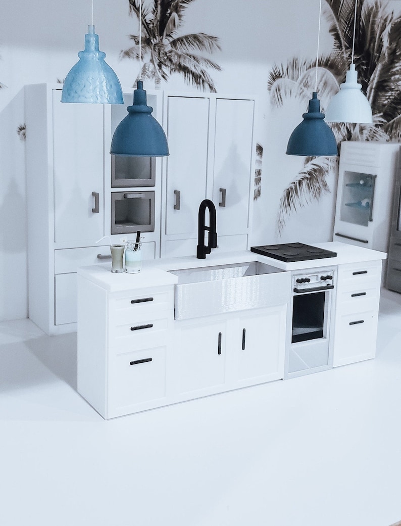 May include: A white kitchen island with a farmhouse sink, a black faucet, and a black stovetop. The island has three drawers and two cabinet doors. There are three pendant lights hanging above the island, two blue and one light blue.