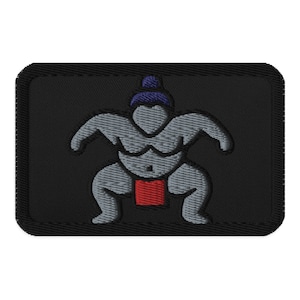 May include: A gray embroidered patch of a sumo wrestler in a fighting stance, wearing a red loincloth and a blue hat.