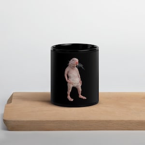 May include: A black ceramic mug with a white, hairless rodent printed on it. The rodent is standing upright with its arms at its sides.