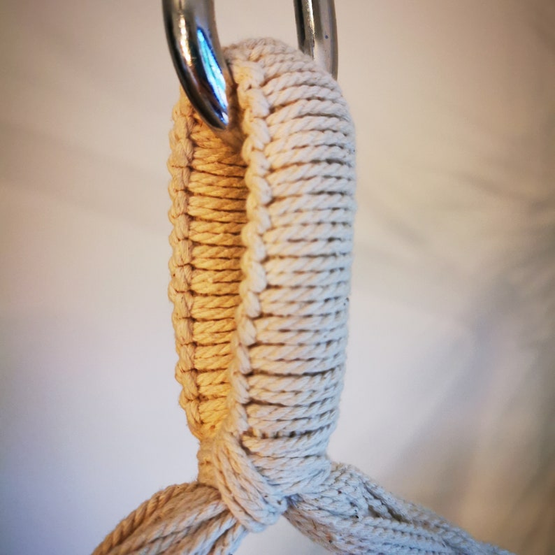 May include: Close-up of a white cotton rope loop hanging from a silver hook. The rope is tightly woven and has a smooth texture.