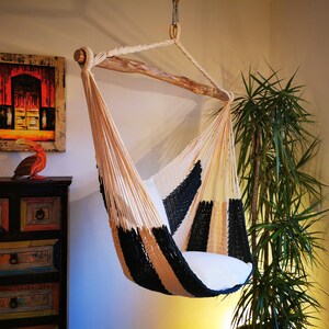 May include: A black and white striped hammock chair with a wooden frame. The hammock is hanging from the ceiling and is made of a soft, woven fabric.