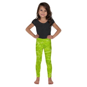 May include: A young girl wearing a black t-shirt and bright green leggings with a white, abstract pattern. The leggings are the focal point, showcasing a vibrant, textured design. The girl is standing with her hands on her hips.