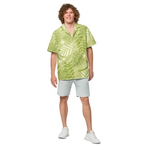 Puede incluir: Una camisa verde de manga corta con botones y un estampado de hojas tropicales. La camisa tiene un cuello blanco y un corte holgado.