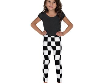 May include: A young person wearing a dark grey t-shirt and black and white chequered leggings. The leggings feature a repeating pattern of black and white squares. The person is standing with their hands on their hips.