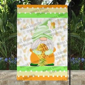 May include: A garden flag featuring a gnome holding a pineapple. The gnome wears a green hat and orange outfit. The background has a pineapple pattern. The flag has orange, green, and yellow stripes with white polka dots. The text "Mama's Basement Creations" is visible.