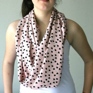 Könnte beinhalten: Ein rosa Schal mit schwarzen Herzen darauf gedruckt. Der Schal wird um den Hals einer Person getragen.