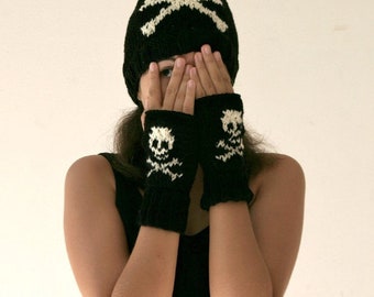 May include: Black knit skull hat and fingerless gloves with white skull designs. The gloves are covering the person's hands.