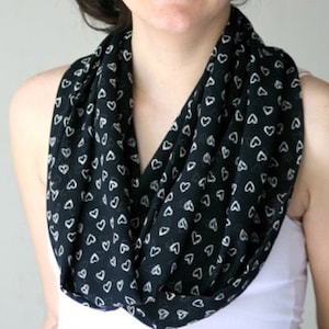 May include: A black infinity scarf with a white heart pattern. The scarf is made of a soft, lightweight fabric and is perfect for adding a touch of style to any outfit.