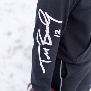May include: Black hoodie with a white signature on the sleeve that says "Tim Bell 12".