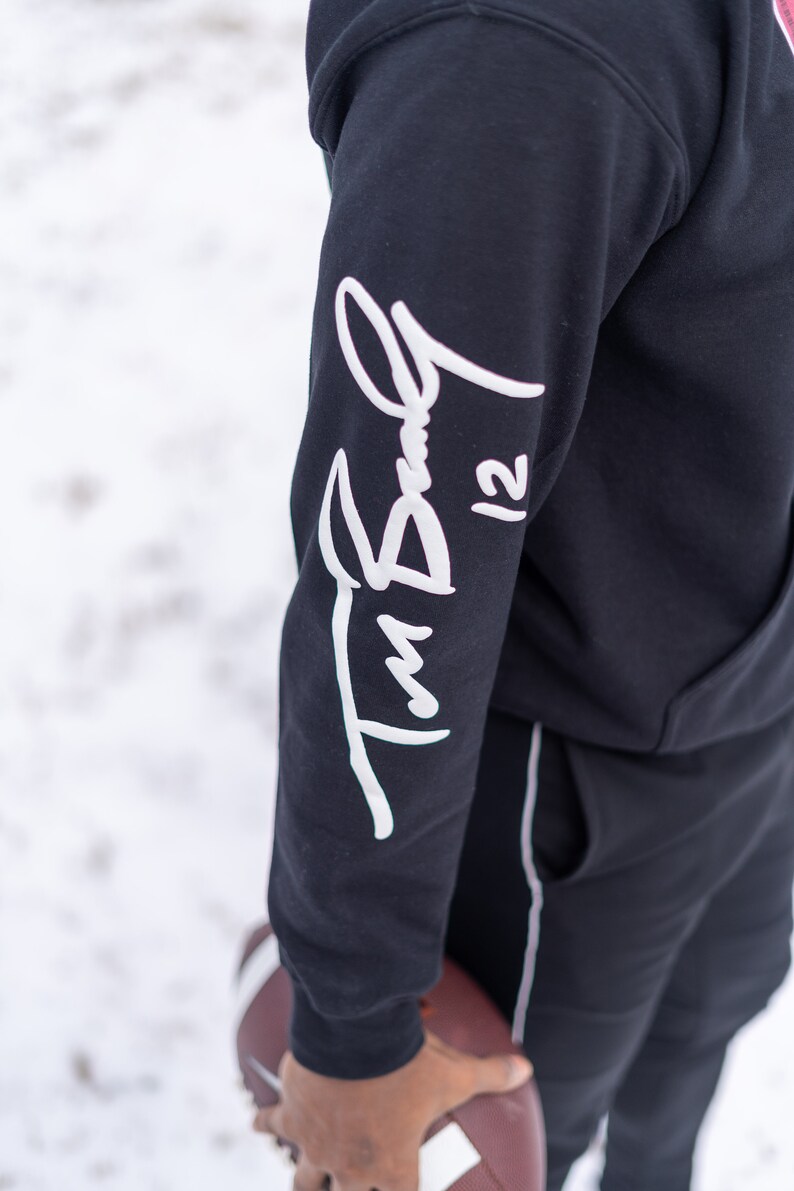 May include: Black hoodie with a white signature on the sleeve that says "Tim Bell 12".