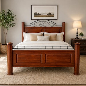 May include: A wooden bed frame with a dark cherry finish. The headboard features a decorative black metal scroll design. The bed is made up with white bedding and pillows. A framed landscape painting hangs above the bed.