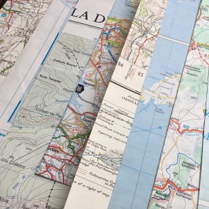 May include: An assortment of folded vintage maps, overlapping to display diverse geographical areas. The maps include road networks, place names, and contour lines, with a variety of colours and text.