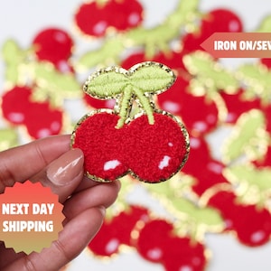 Może przedstawiać: Czerwone i zielone łatki z wiśniami do prasowania lub przyszywania z dodatkami złotych brokatów. Tekst "IRON ON/SEW ON" jest widoczny na zdjęciu.