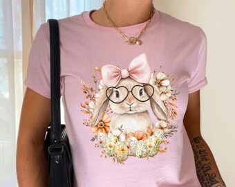 May include: Pink t-shirt with a graphic of a bunny wearing glasses and a bow. The bunny is surrounded by flowers and eggs.