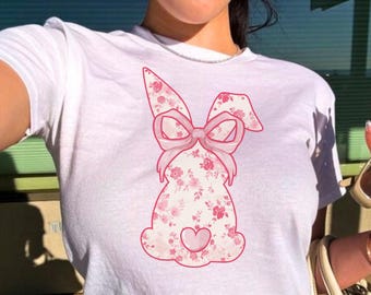 May include: White cropped t-shirt with a pink floral bunny graphic. The bunny has a pink bow and a pink heart on its chest.